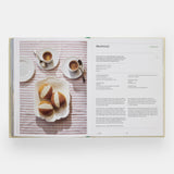 Calimia Home The Regional Italian Cookbook book open to a spread showing a sweet bun recipe on a striped tablecloth.