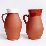 Two handmade Calimia Home terracotta pitchers with white and dark red glazed rims against a plain white background.