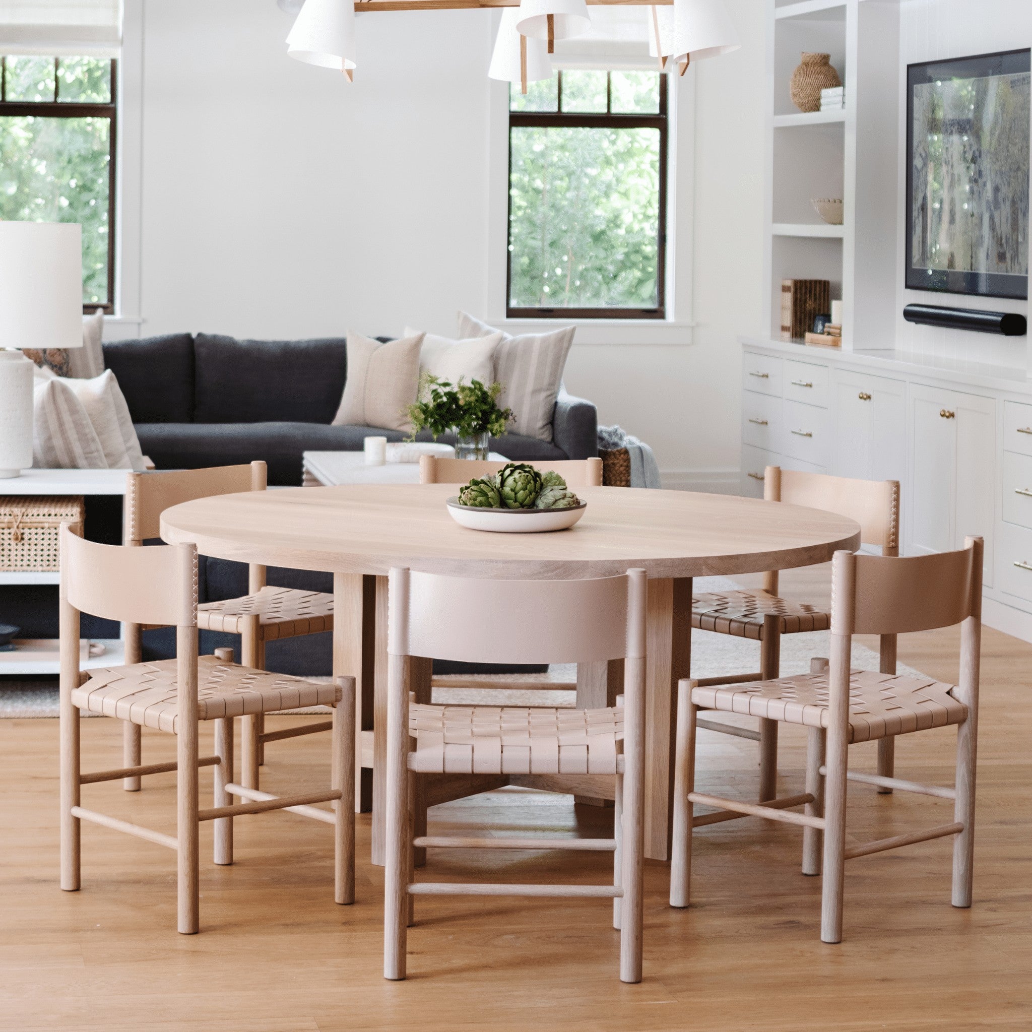 Valencia X Dining Table by Grove & Anchor in natural oak, round top with sculptural X-base legs, styled in a bright dining room with woven-seat chairs