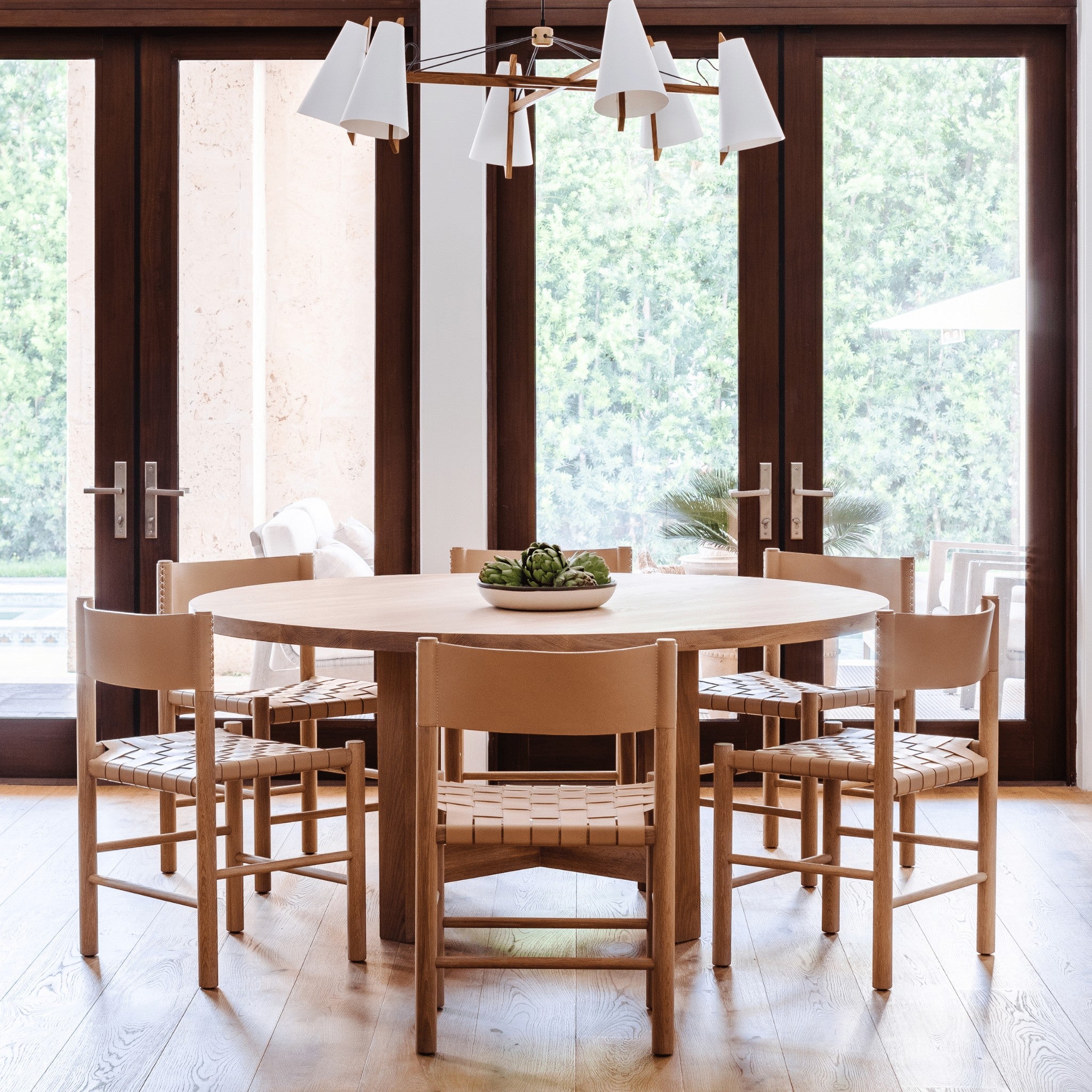 Valencia X Dining Table in natural oak by Grove & Anchor with a sculptural X-base, styled near French doors with woven-seat chairs