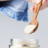 Calicutts vanilla bean sugar being poured from a wooden measuring spoon into a glass jar