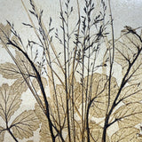 Close-up of a vintage ceramic botanical wall tile showing grass seed heads and leaf veins pressed in relief with an iron-toned wash