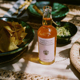 Flamingo Estate Persimmon Vinegar on a sunlit linen tablecloth beside green ceramic bowls of tortilla chips and bright guacamole.