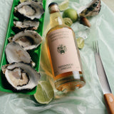 Flamingo Estate Persimmon Vinegar perches on tissue paper next to a tray of freshly shucked oysters on the half shell with lime wedges.