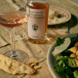 Persimmon Vinegar from Flamingo Estate joins a coupe of rosé and a green salad with shaved cheese on a linen-set table at golden hour.