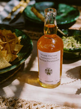 Flamingo Estate Persimmon Vinegar on a sunlit linen tablecloth beside green ceramic bowls of tortilla chips and bright guacamole.