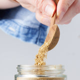 Calicutts Za'atar spice blend being poured from a wooden spoon into a glass jar.